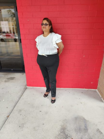 Plus size woman wearing black pants and white bodysuit in front of a red wall